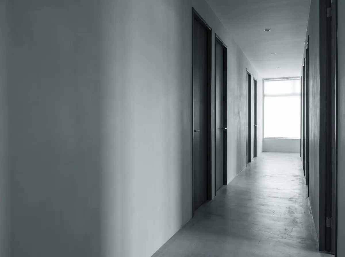 A quiet clinic corridor with doorways to treatment rooms and soft light falling from one end.